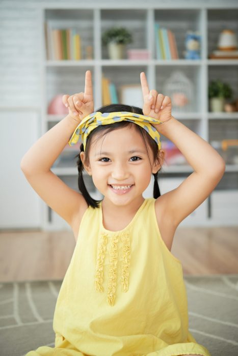 Portrait of smiling little girl making cow horns with her hands